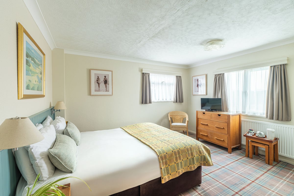 A bedroom with a bed, a dresser, a television, and a window with curtains.