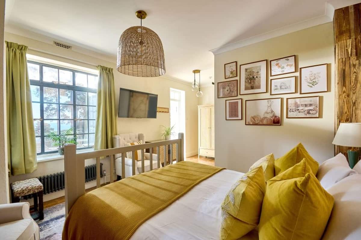 A bedroom with a bed, a wooden headboard, a window with curtains, a wall-mounted TV, and framed pictures.
