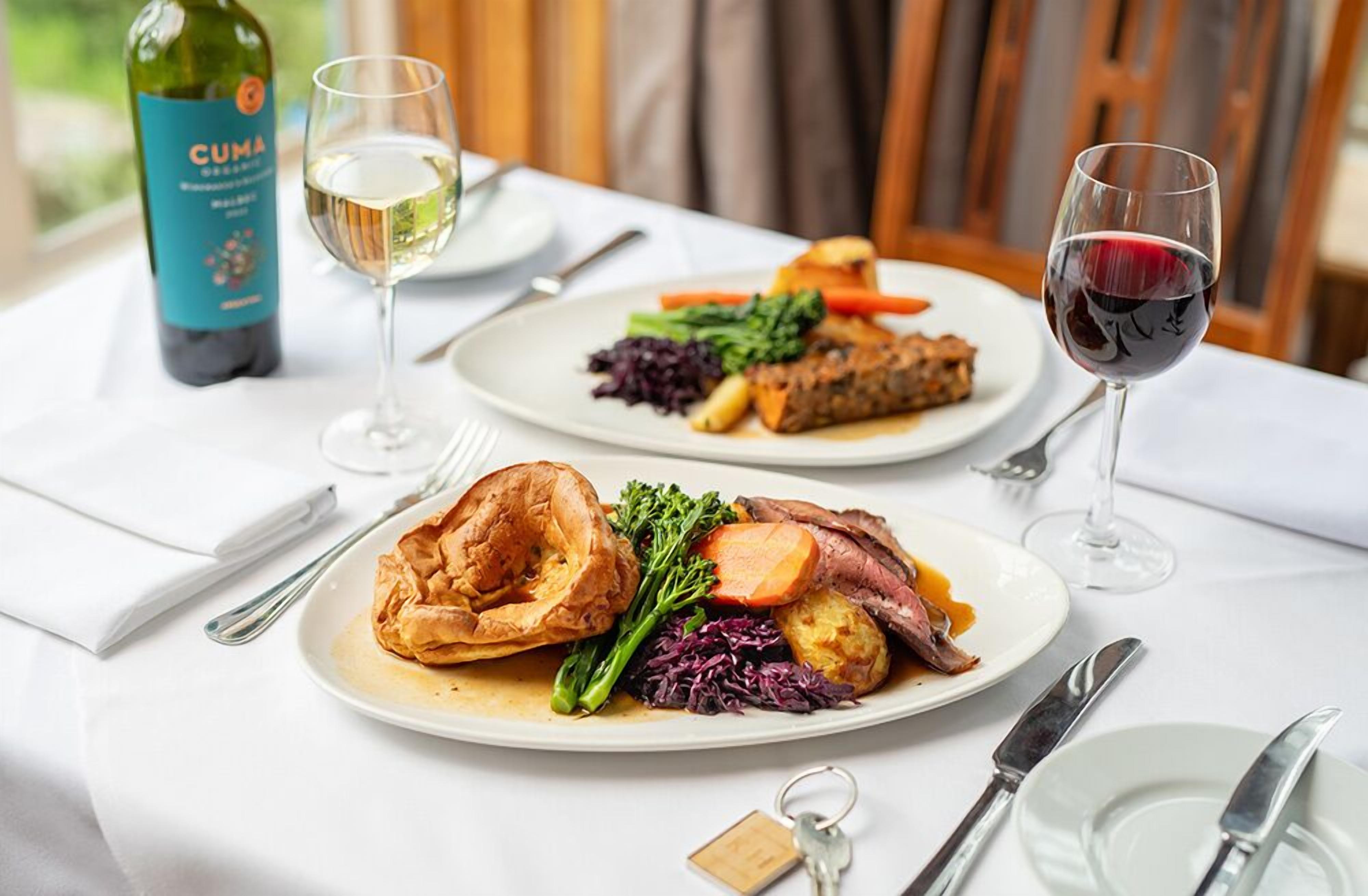 Une table à manger avec des assiettes remplies de nourriture, des verres à vin et une bouteille de vin CUMA.