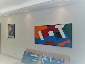Um interior moderno com uma grande pintura abstrata, uma moldura com fotografia e um sofá com almofadas estampadas.