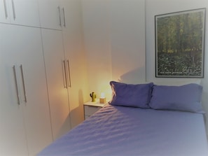Quarto com uma cama, uma mesa de cabeceira, um cacto e um quadro na parede.