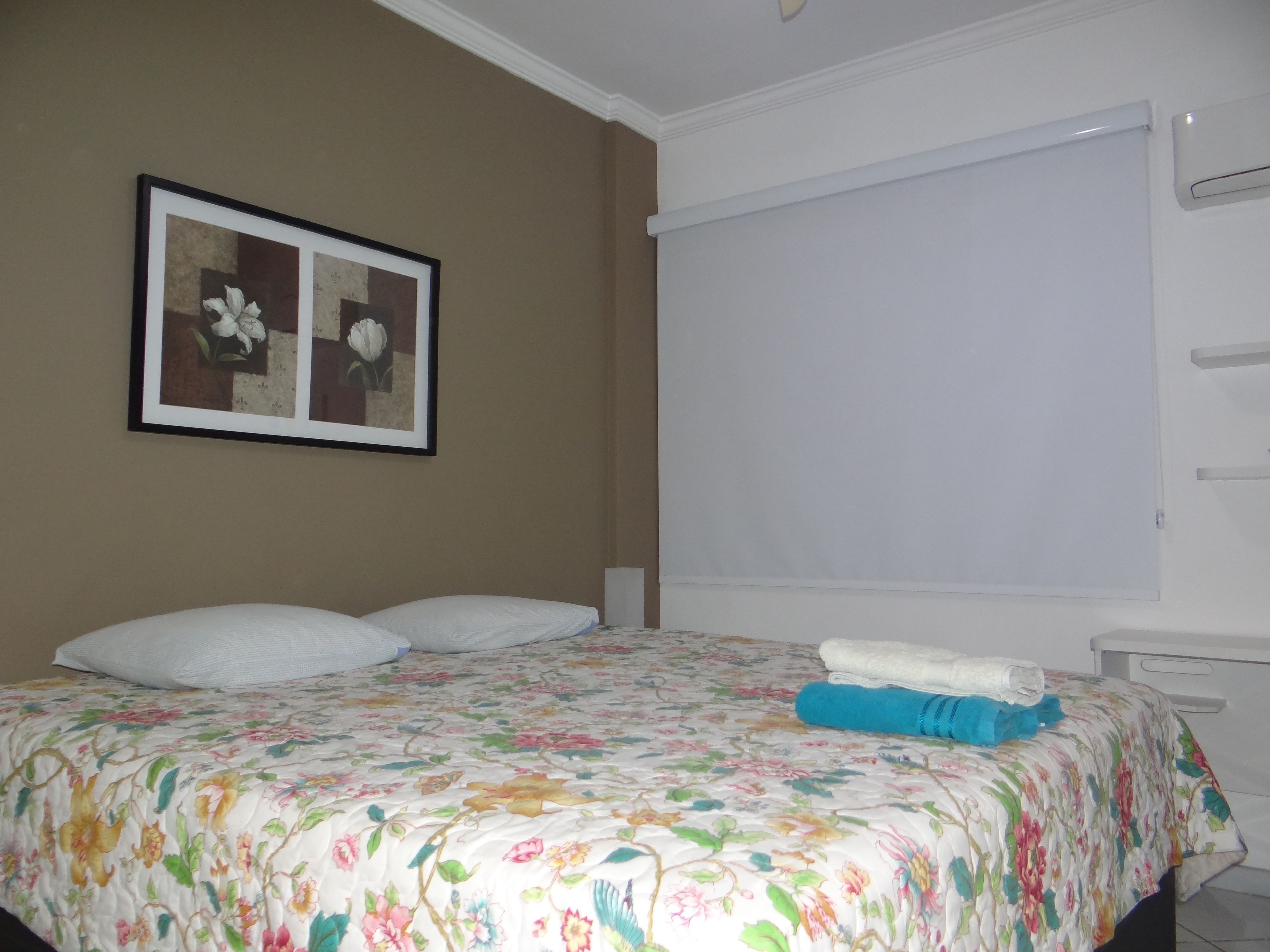A bedroom with a floral bedspread, a framed picture on the wall, and a white ceiling.