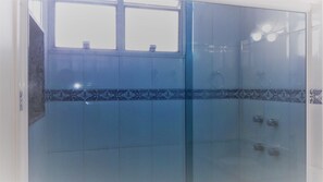 A bathroom with a glass shower enclosure, a window, and a decorative tile border. - Beautiful Apartment in Ipanema (Rio de Janeiro)