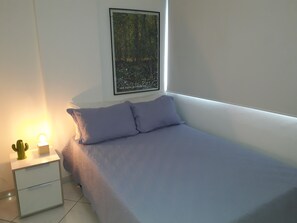 A bedroom with a bed, a nightstand, a lamp, and a framed picture on the wall. - Beautiful Apartment in Ipanema (Rio de Janeiro)