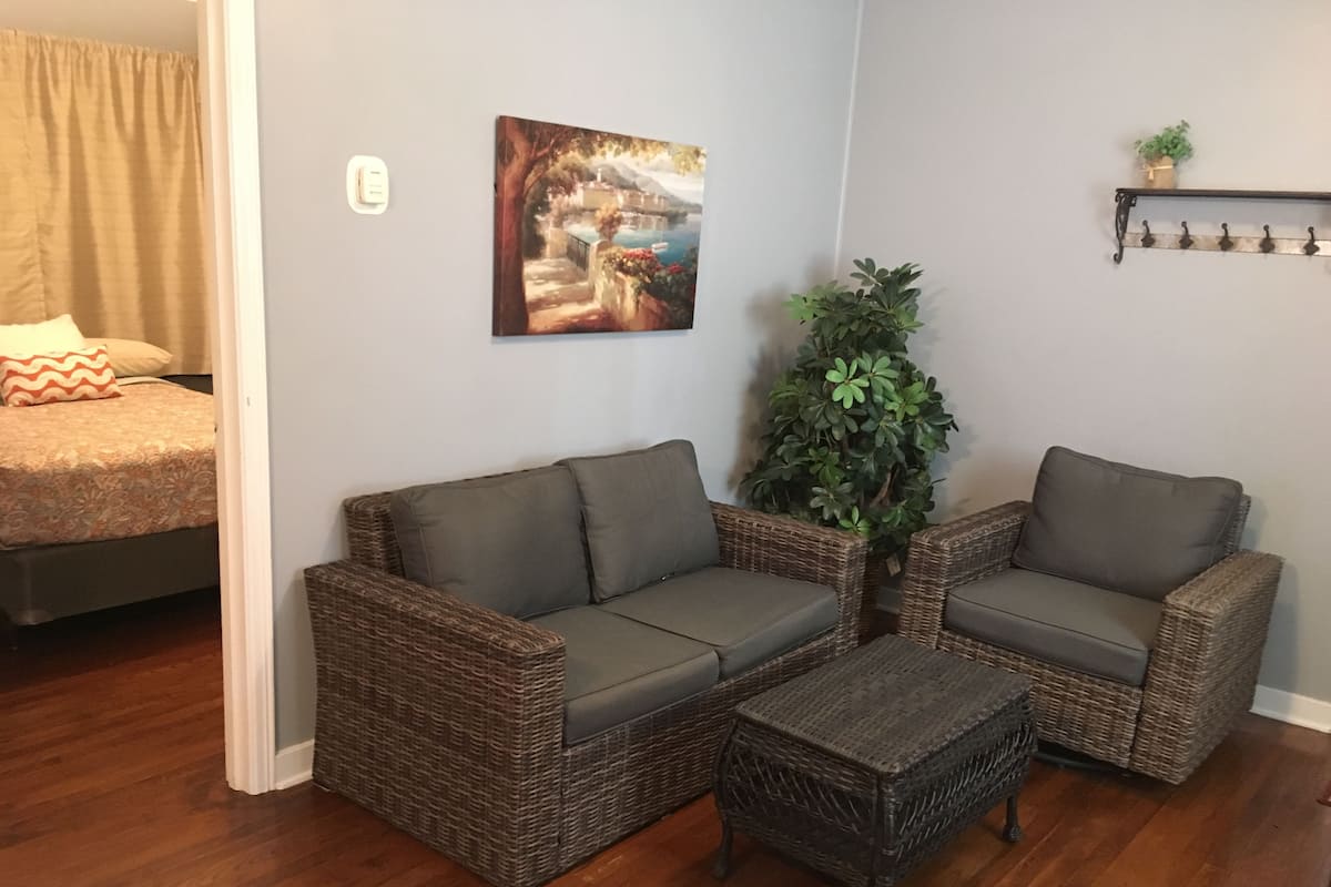 A living room with a sofa set, a small table, a potted plant, and a painting on the wall.