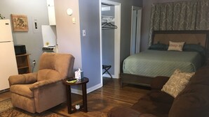 Una habitación de hotel con una cama, un sofá, una silla, una mesita con una caja de pañuelos, un microondas y un refrigerador.