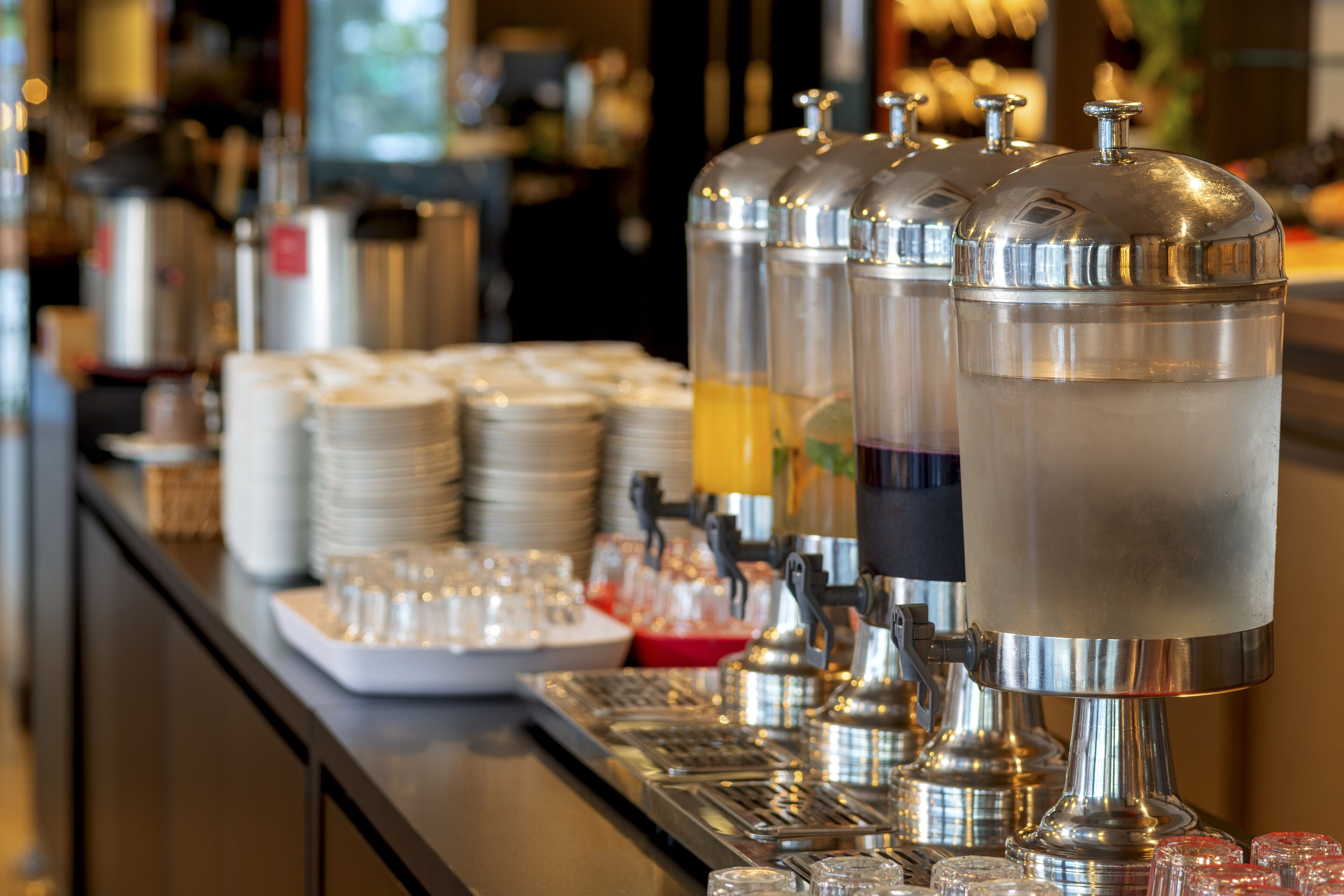 A bar area with multiple beverage dispensers, stacked plates, and glasses.