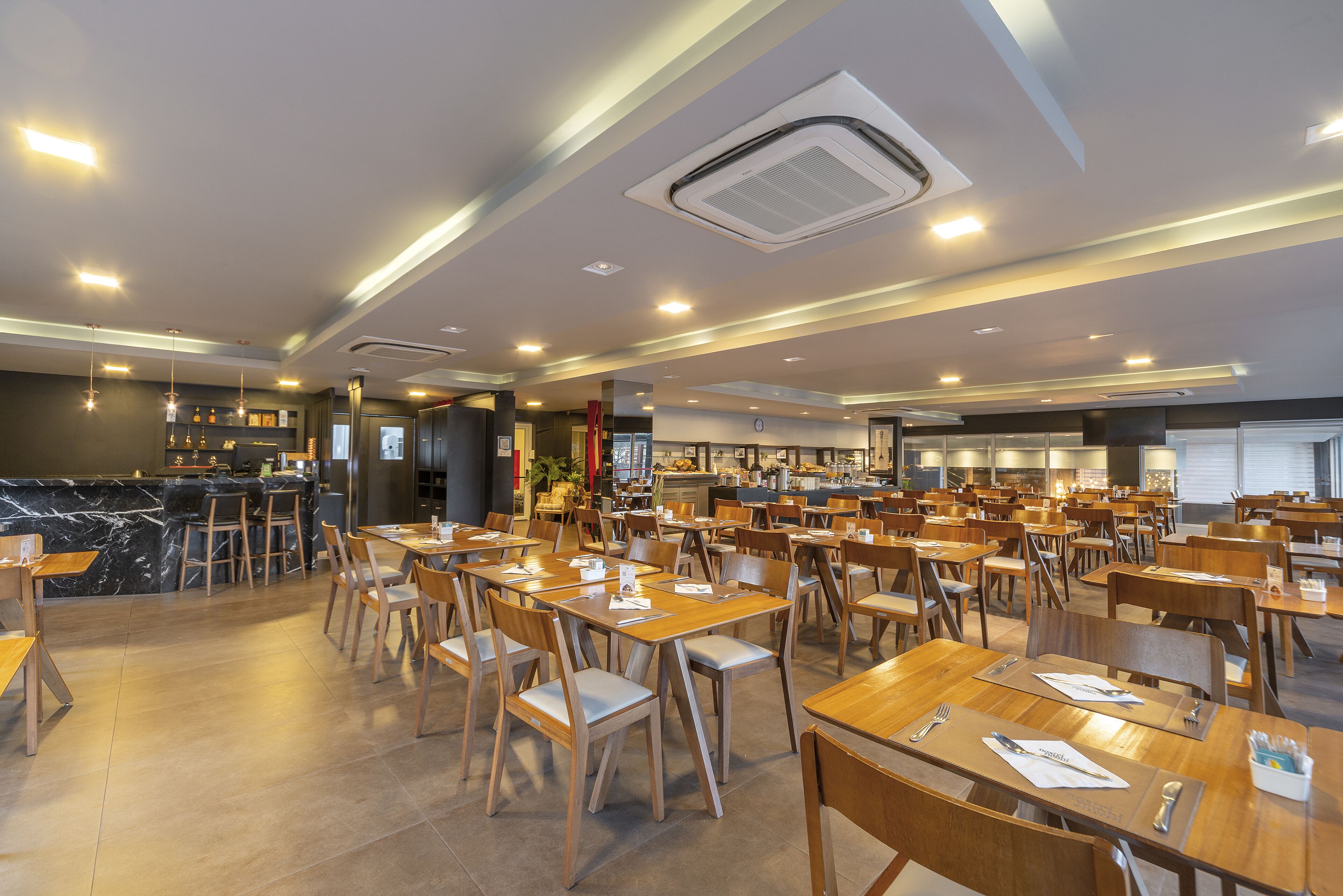 A spacious dining area with multiple tables and chairs, a bar area, and a kitchen in the background.