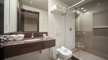 A modern bathroom with a sink, mirror, and toilet. There are towels on the sink and a glass shower enclosure.
