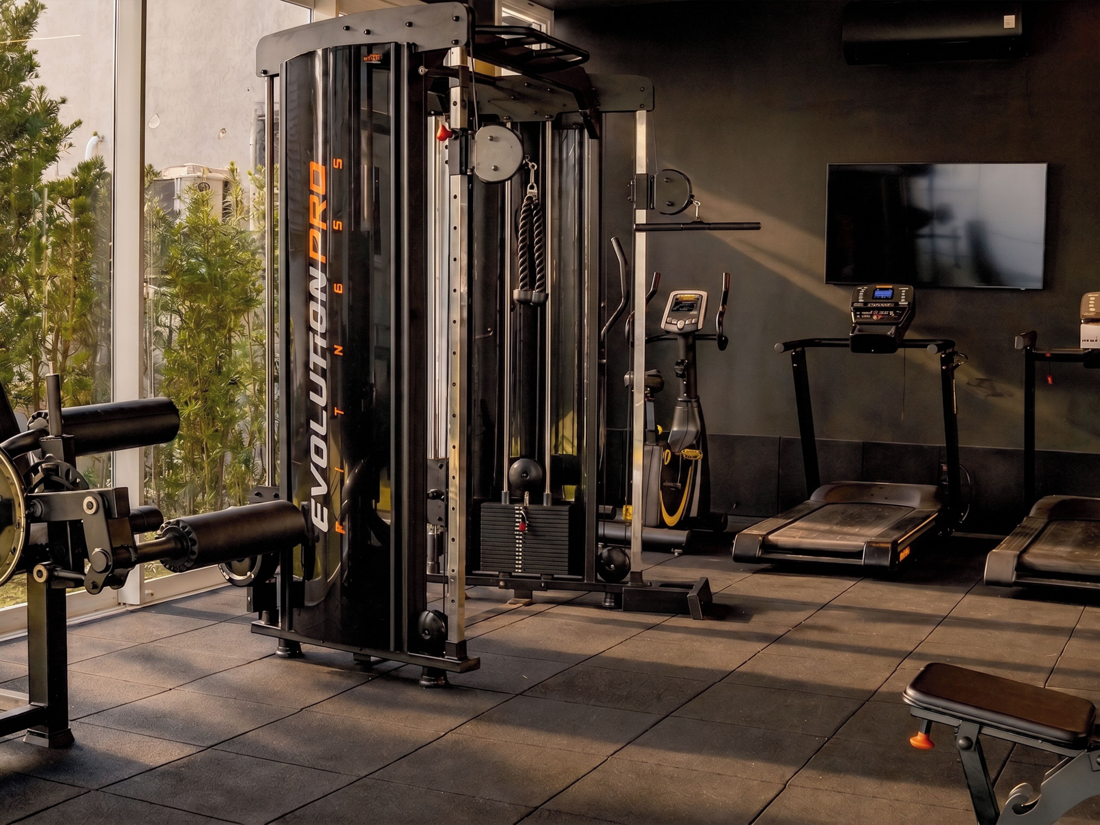 Une salle de sport équipée de matériel d’exercice, d’un tapis de course et d’un téléviseur fixé au mur.