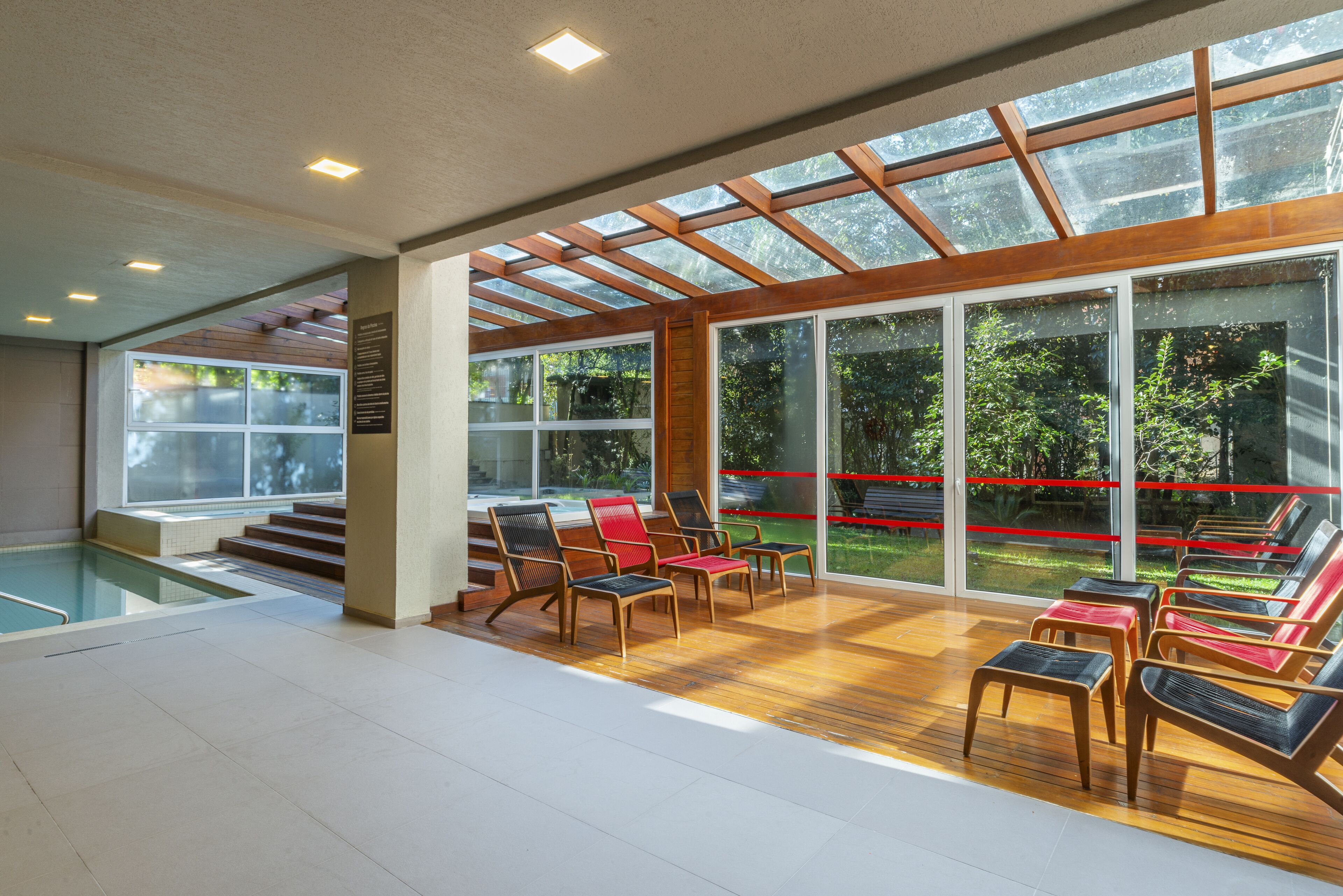 A modern indoor pool area with a glass ceiling, wooden flooring, and multiple lounge chairs.
