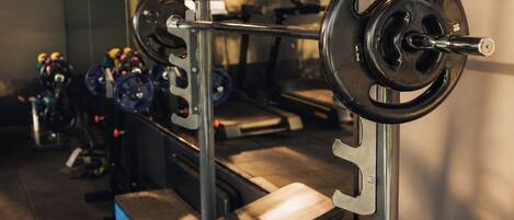 Un gimnasio con equipamiento de levantamiento de pesas, bancos y cintas de correr.
