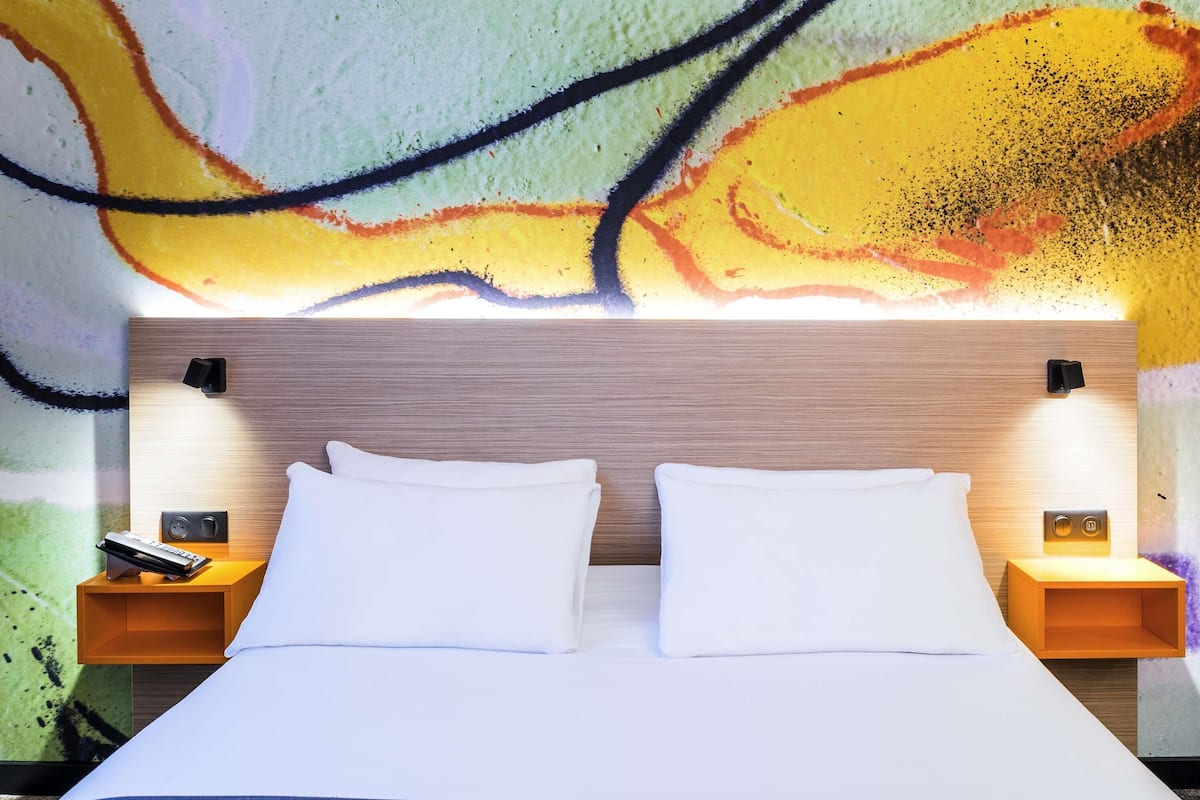 Una habitación de hotel con una cama grande, dos mesitas de noche y un llamativo mural abstracto en la pared.