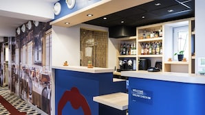 Ein Empfangsbereich mit blauer Rezeption, einer wandmontierten Kaffeemaschine und einer Wand mit einer großen roten Bogenform.