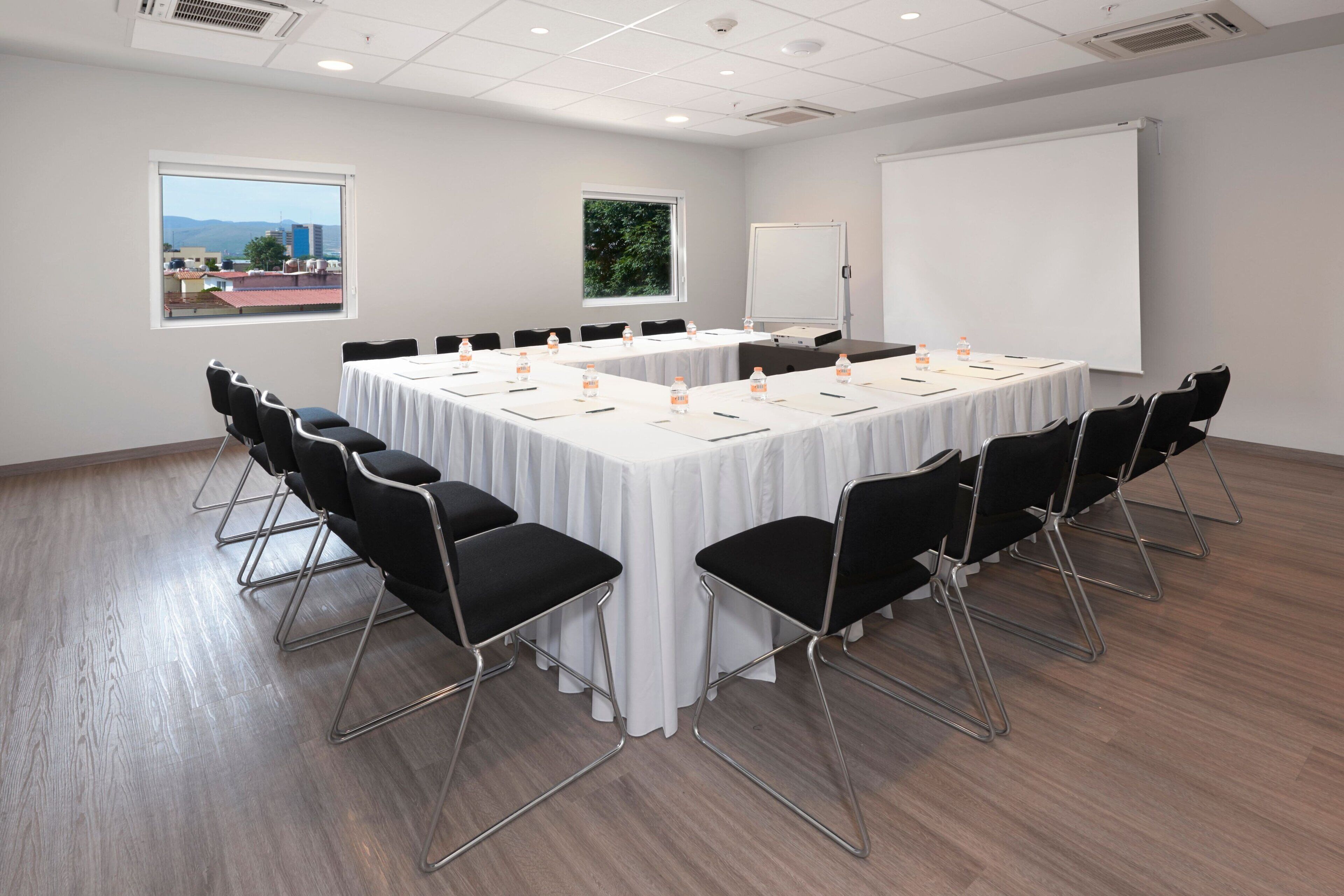 Una sala de conferencias con una gran mesa, sillas negras, una pizarra y una pantalla de proyector.