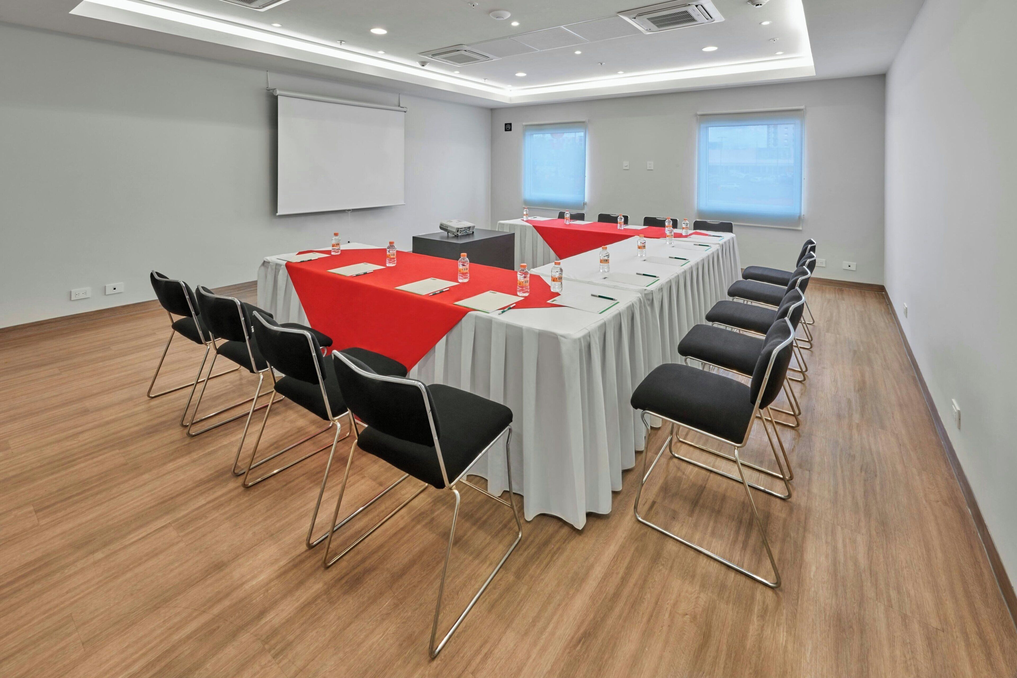 Un salón de conferencias con una larga mesa, sillas negras y una pantalla para proyector.