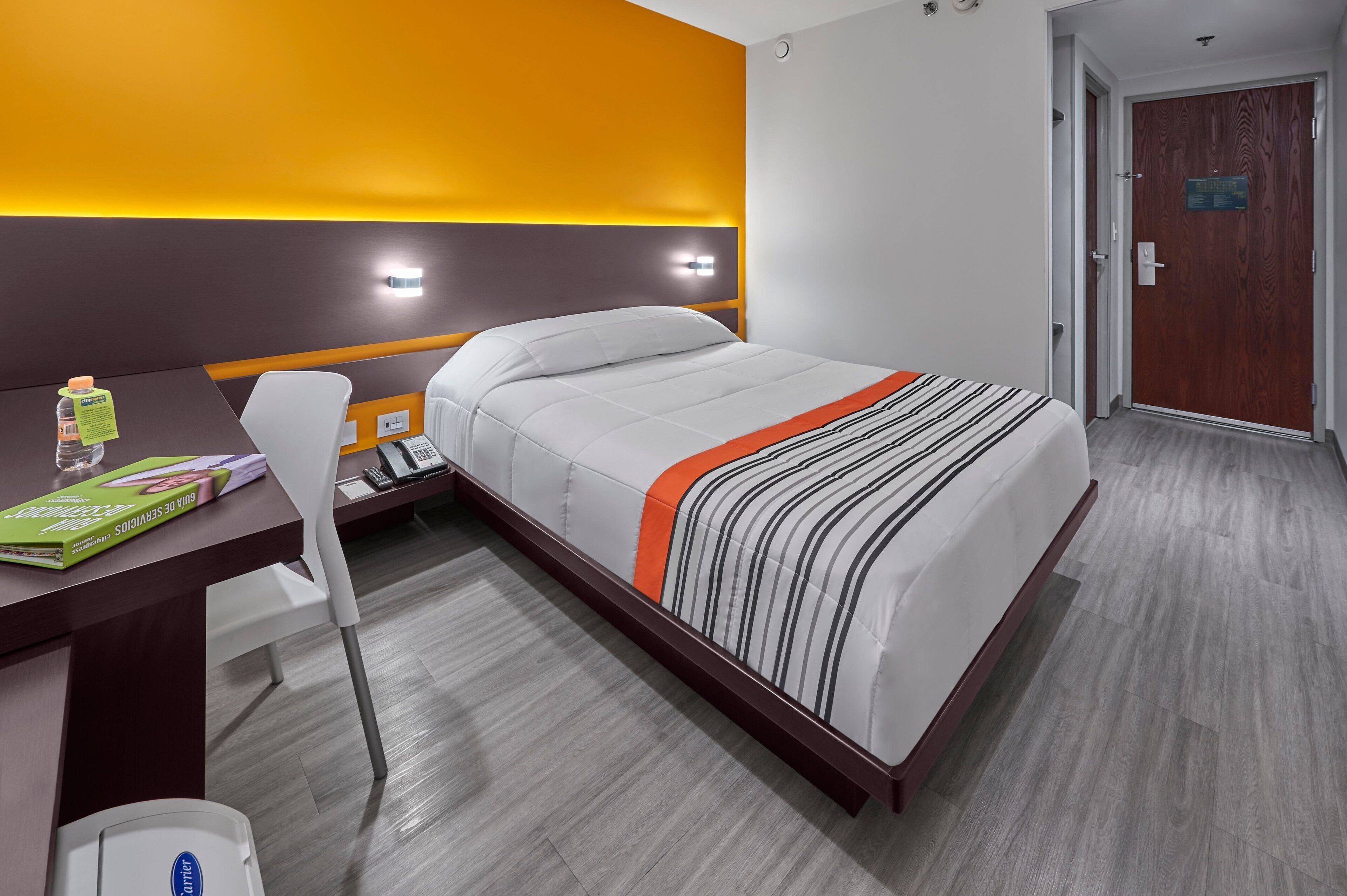 Een hotelkamer met een bed, een bureau met stoel, een telefoon en een waterfles.