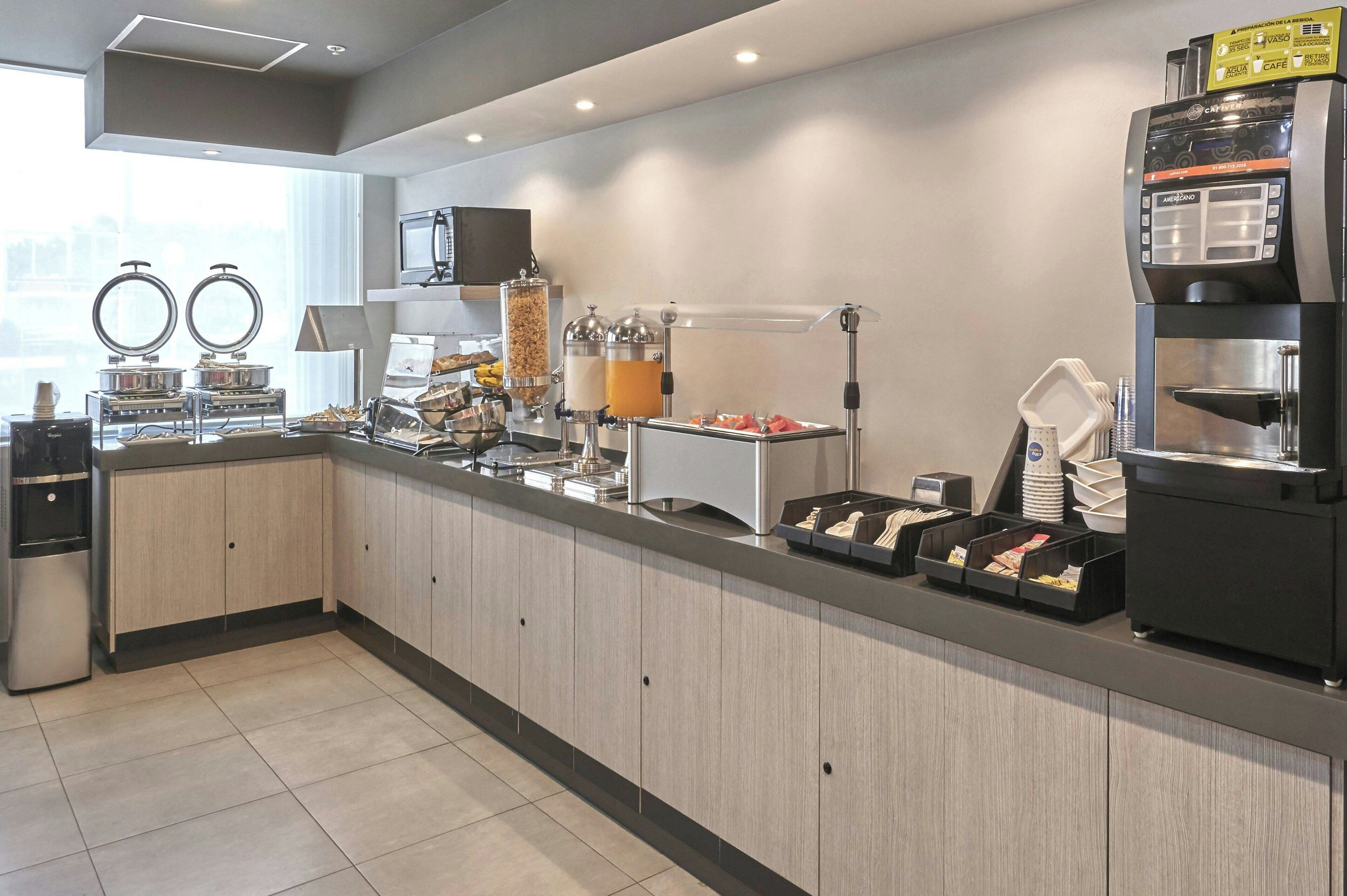Un comptoir-bar moderne, équipé d’une machine à café, d’un distributeur de jus et de différents récipients pour aliments.