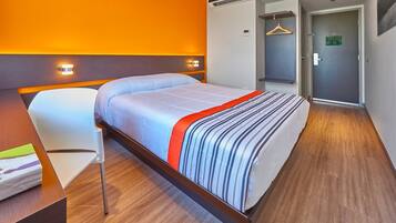 A hotel room with a bed, a desk, a chair, and a wardrobe.