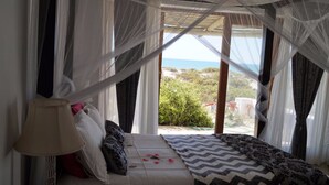 A bed with a canopy, a bedside lamp, and a view of the outdoors. - Escape Beach House (Bergrivier)