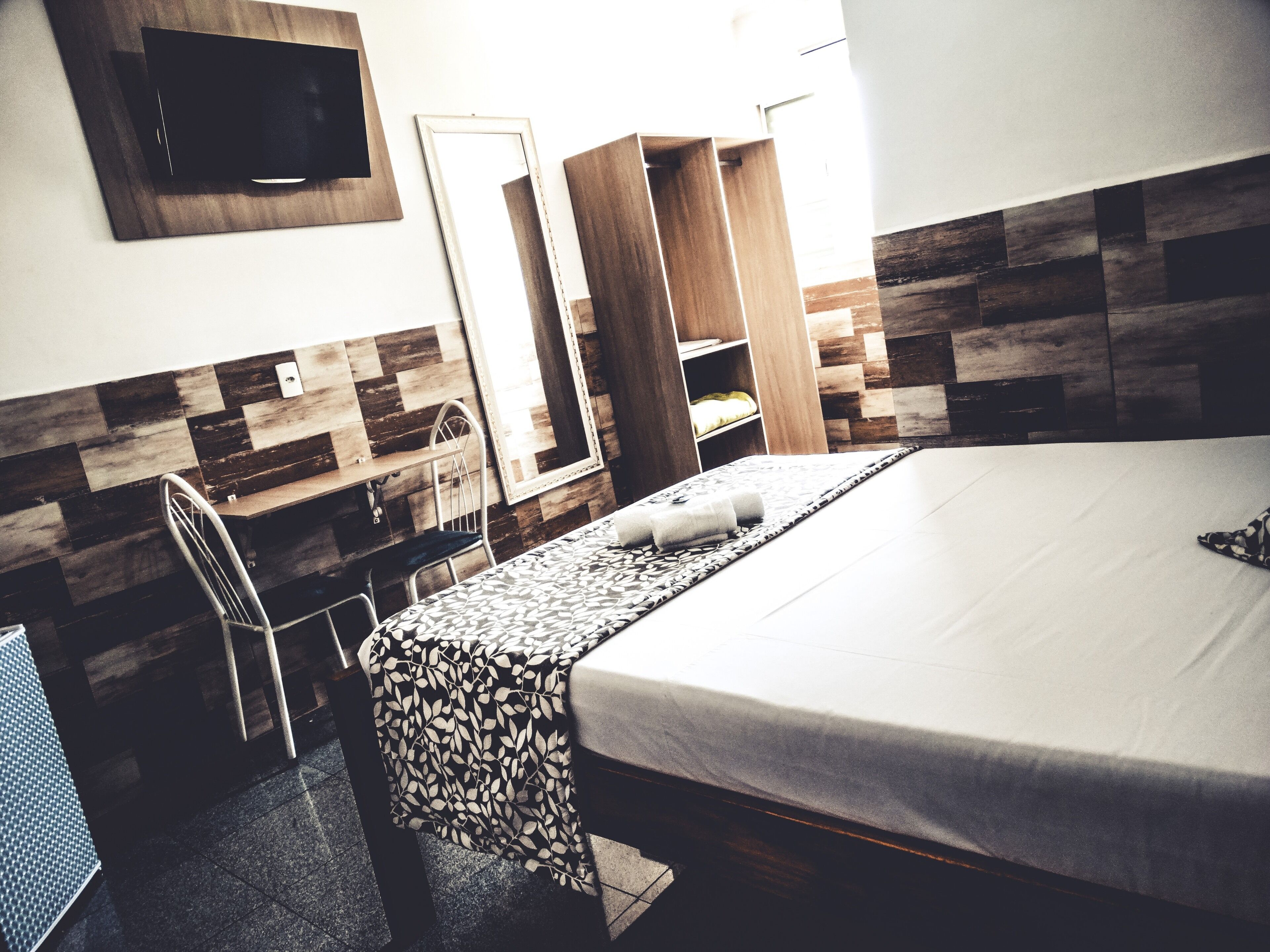 A hotel room with a bed, a desk, a chair, and a wardrobe.