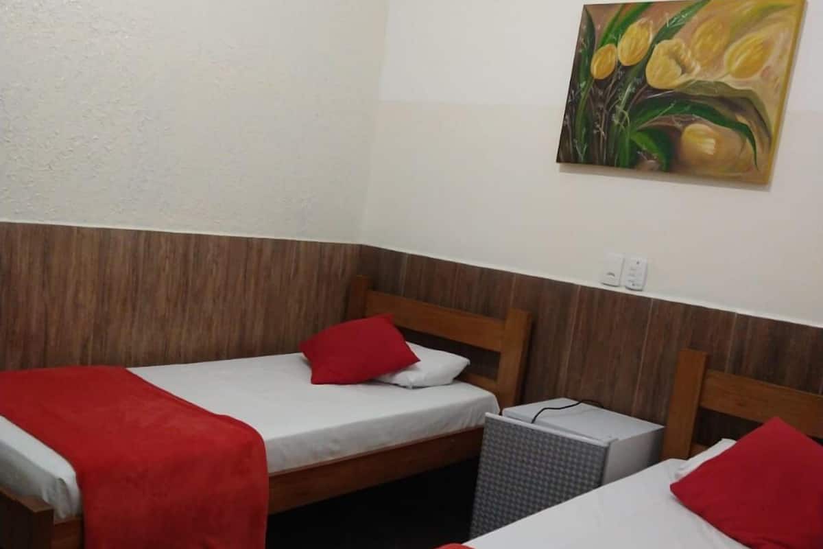Una habitación de hotel pequeña con dos camas individuales, cada una con una manta y almohada rojas, un cabecero de madera y un cuadro en la pared.