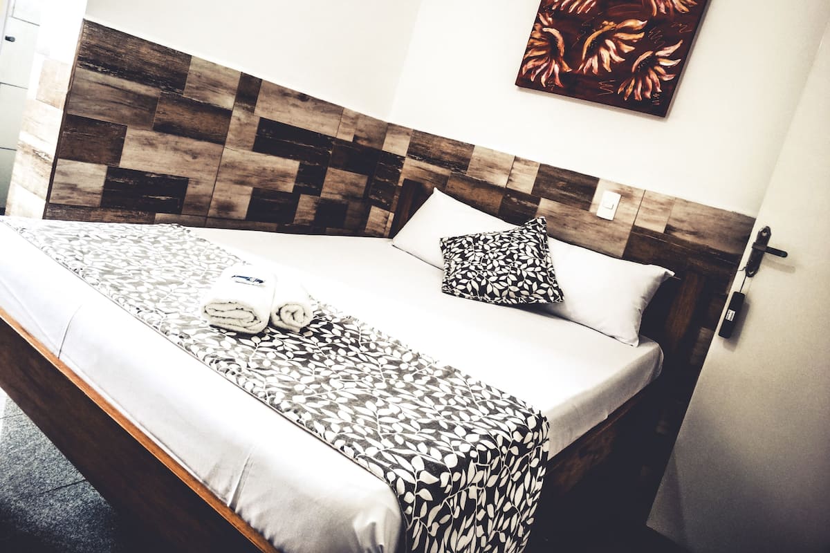 Una cama bien hecha con ropa de cama estampada, un cabecero de madera y una obra de arte colgada en la pared.