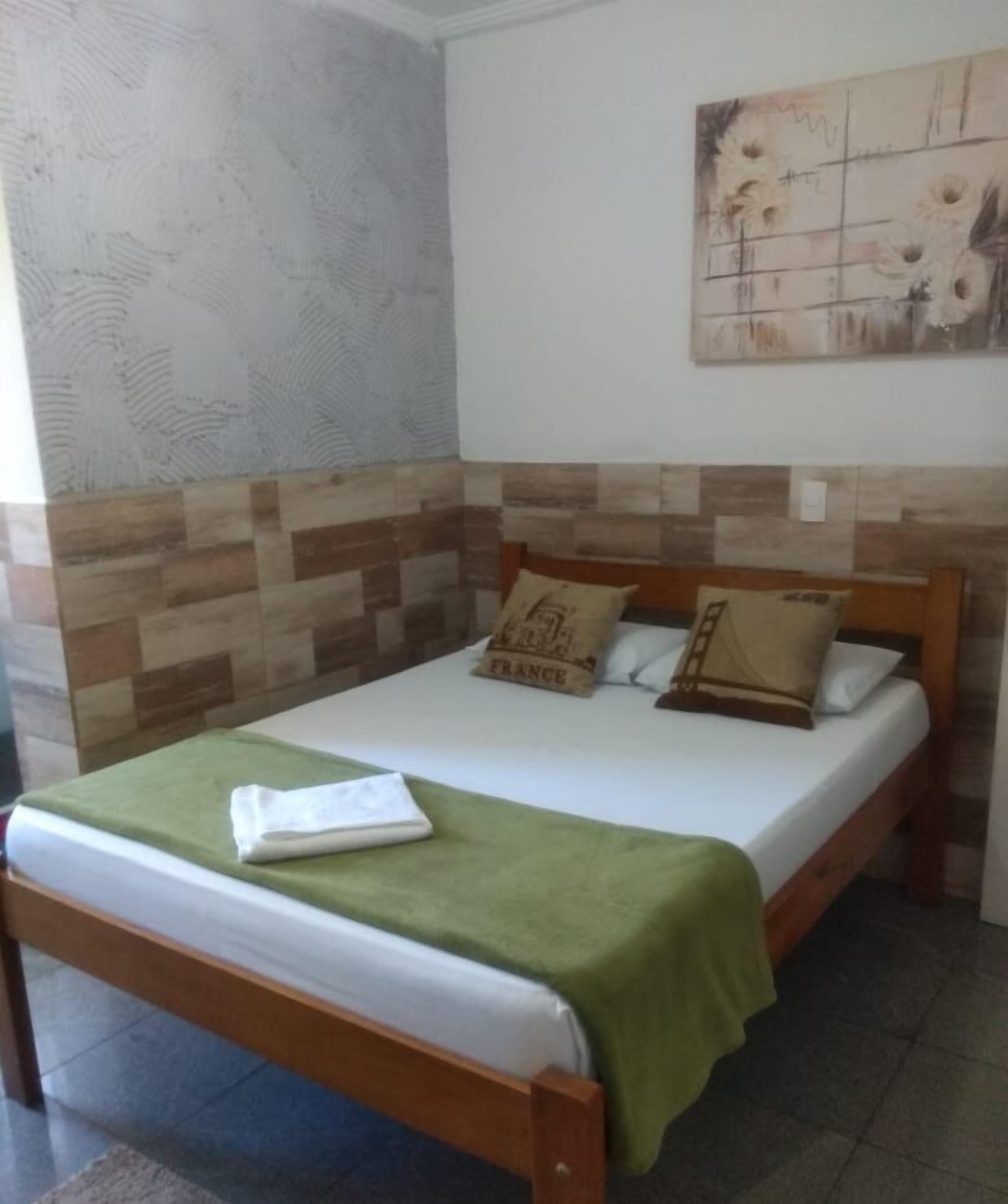 A single bed with a green blanket, a wooden headboard, and two pillows with text.