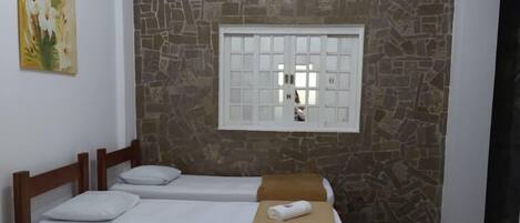 A hotel room with two single beds, a stone wall, a window with bars, and a television.
