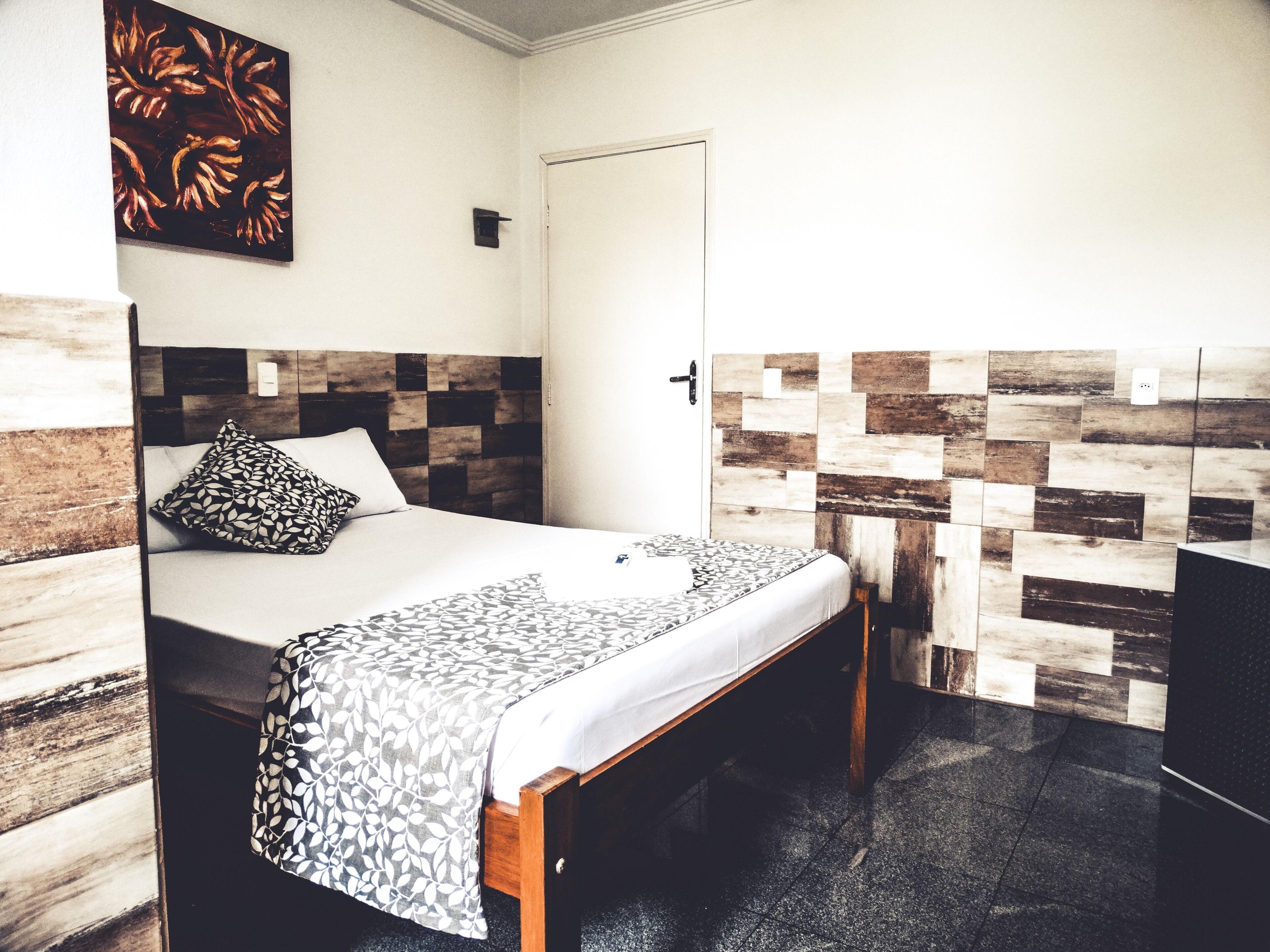 A hotel room with a bed, a wooden headboard, a patterned wall, and a door.