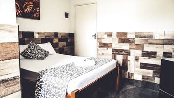 A hotel room with a bed, a wooden headboard, a patterned wall, and a door.