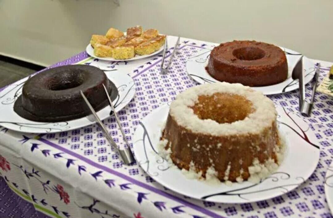 A table with three cakes on plates, a cake server, and a patterned tablecloth.