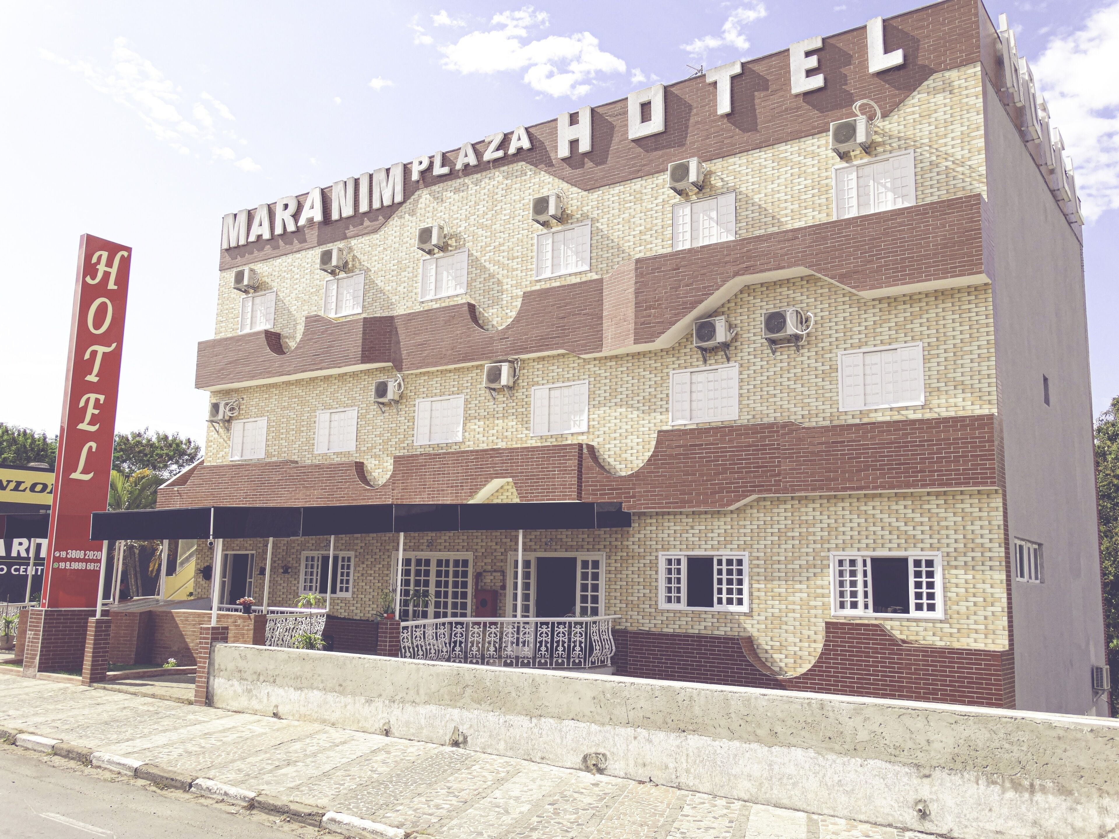 A hotel with a distinctive facade featuring a mix of brick and beige tiles, multiple windows with white shutters, and air conditioning units.