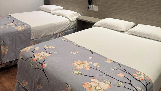 A hotel room with two beds, each with floral bedspreads, a wooden headboard, and a bedside table with a phone and outlet. - Motel Chez Nous (Laval)