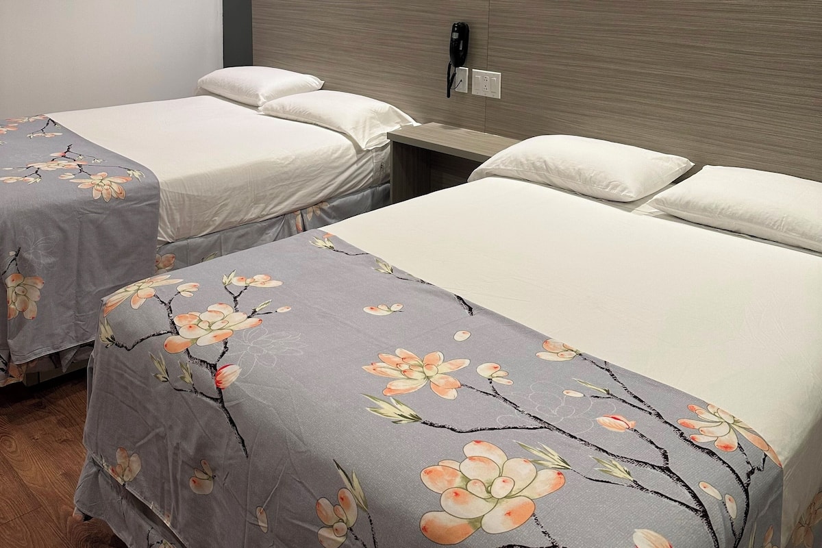 Habitación de hotel con dos camas, cada una con cubrecamas florales, cabeceros de madera y mesitas de noche con teléfono e enchufe.