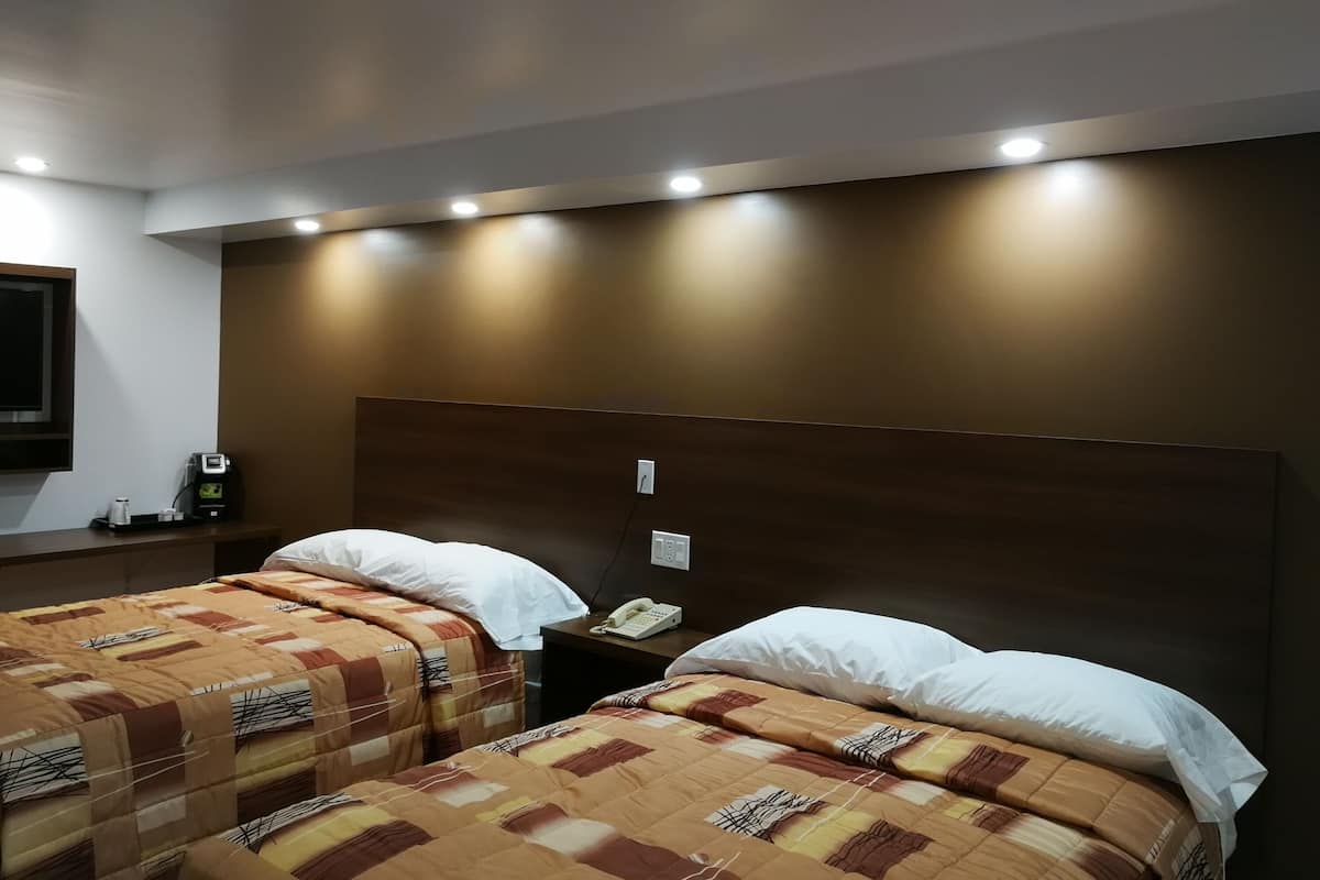 Una habitación de hotel con dos camas, cada una con una colcha estampada, una mesita de noche con teléfono y una lámpara de pared.