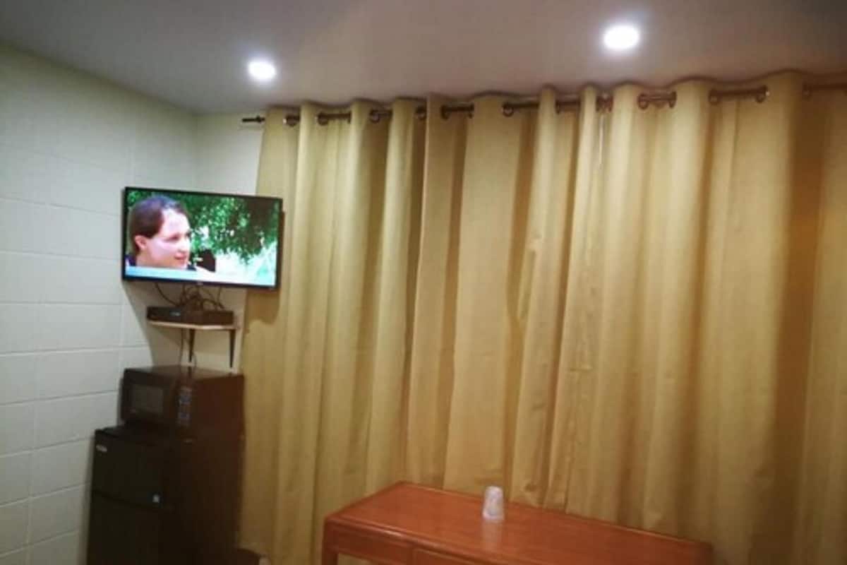 Una habitación con una televisión montada en la pared, un escritorio de madera y una cama con ropa de cama estampada.