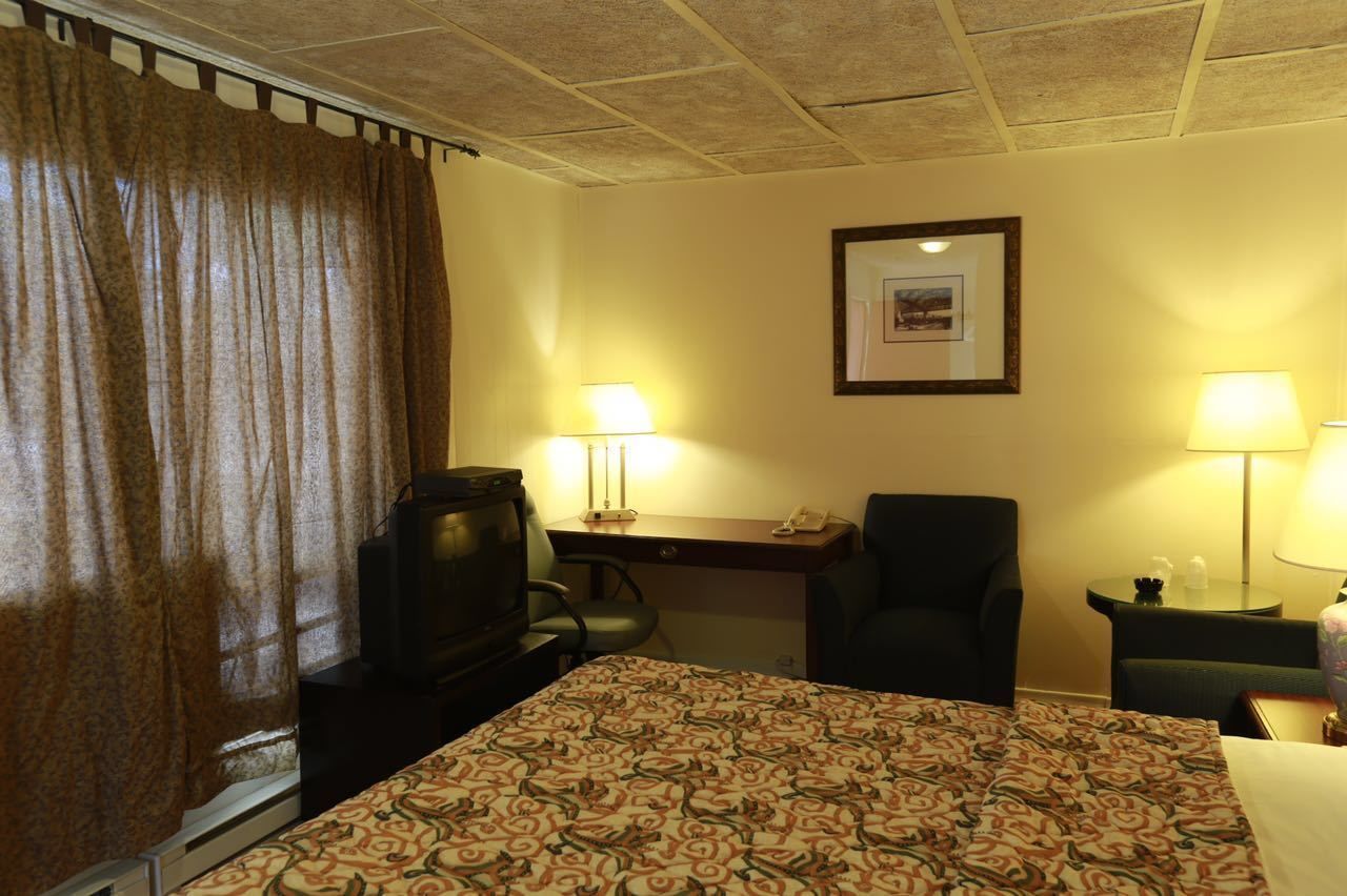 Une chambre d’hôtel comprenant un lit, deux chaises, un bureau, une télévision et deux lampes.