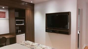 A bedroom with a bed, a TV mounted on the wall, a microwave, and a small desk with a chair.