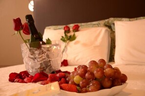 A bed with a bottle of champagne, ice, strawberries, and grapes on a white bedspread. - Ideali Hotel (Ribeirão Preto)