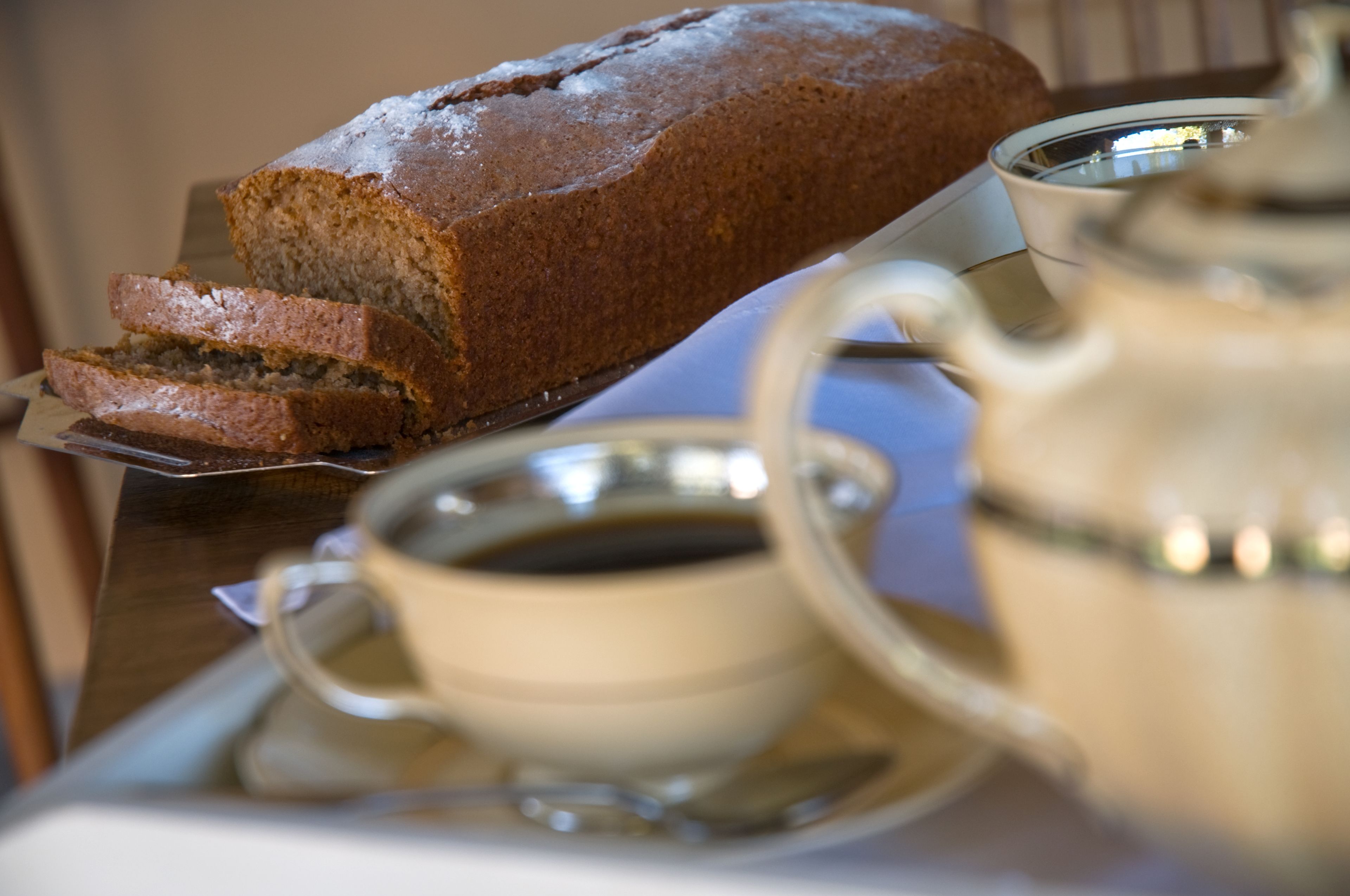 Una hogaza de pan sobre un plato, una taza de café y un calentador de agua en una bandeja.