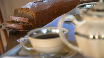 Una hogaza de pan sobre un plato, una taza de café y un calentador de agua en una bandeja.
