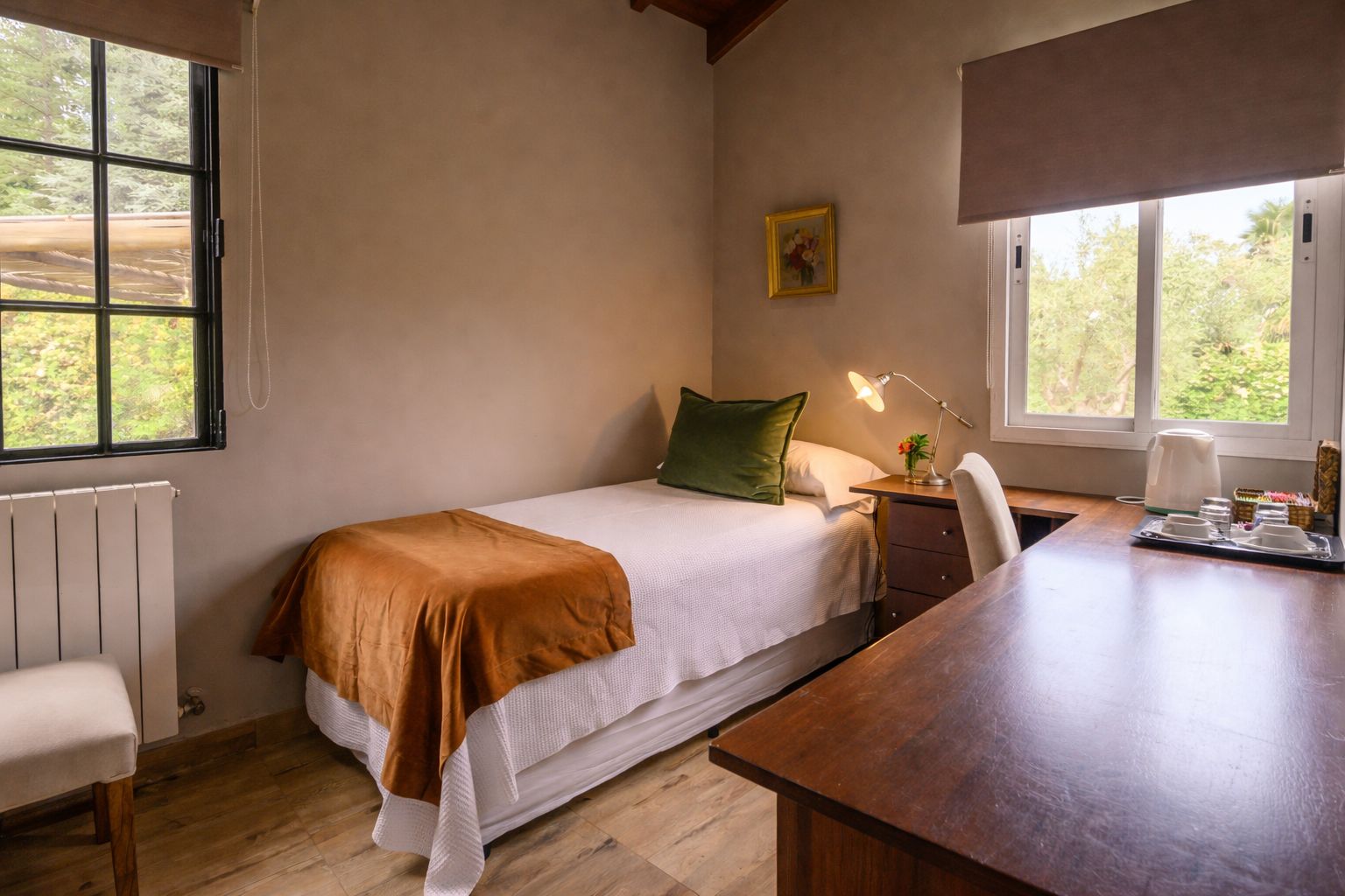 A bedroom with a bed, bedside table, lamp, and a view of greenery outside.