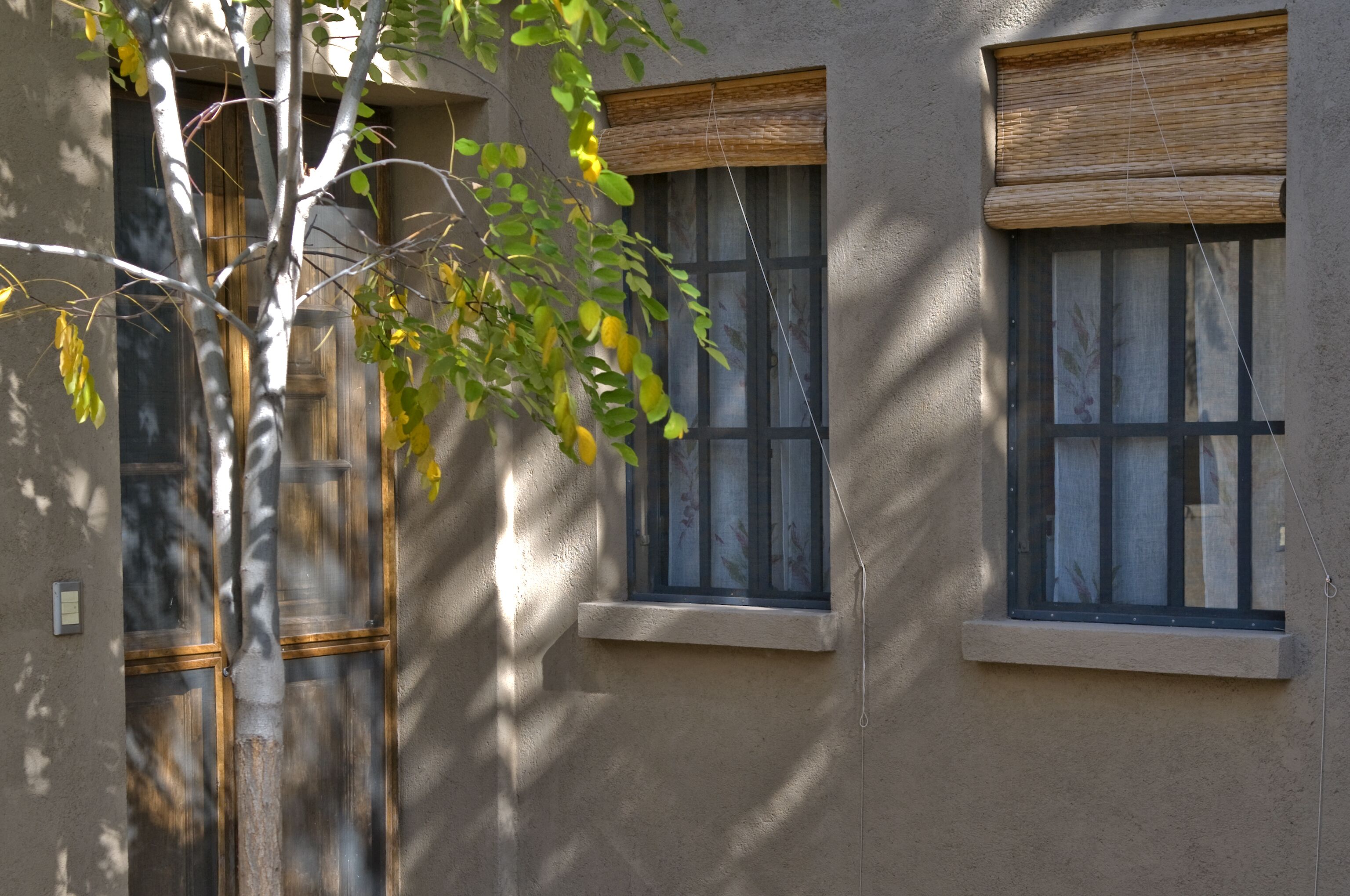 A building with two windows, one with a wooden blind and another with a metal blind.