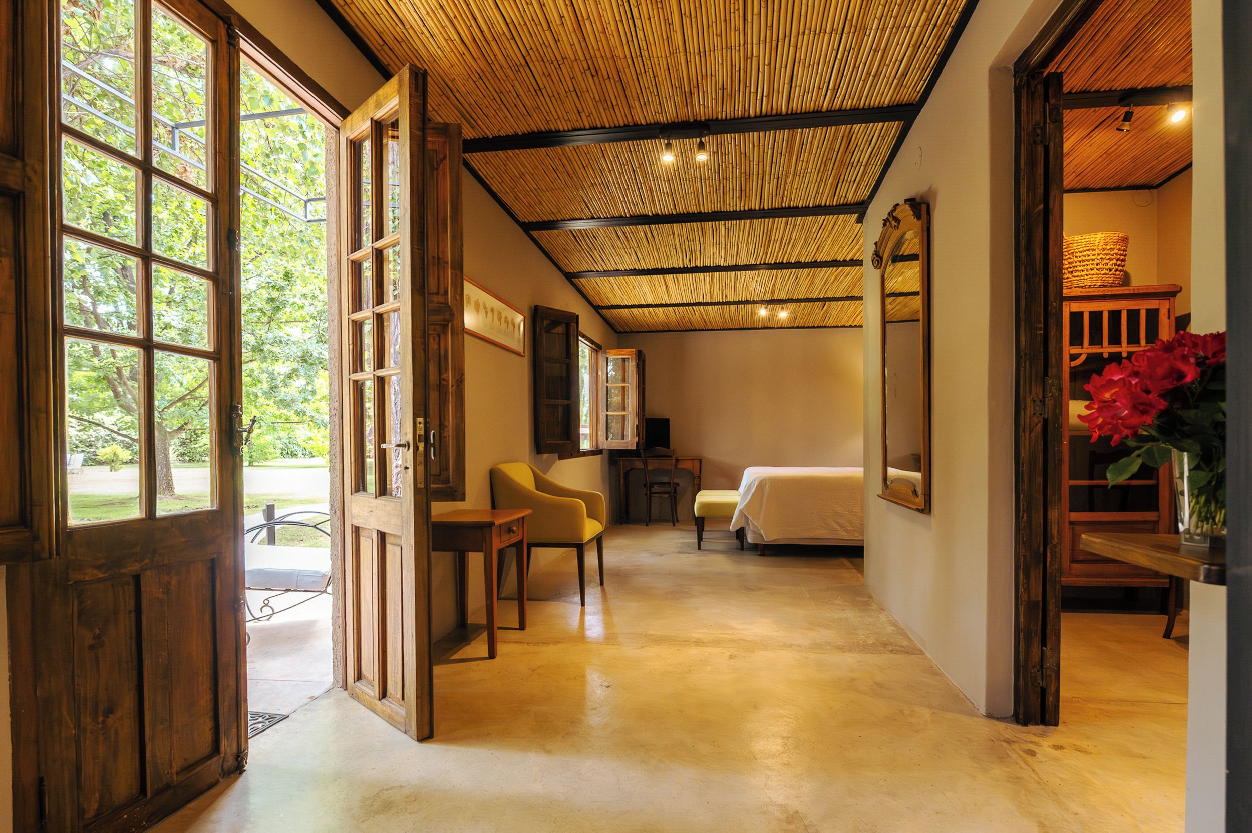 Una habitación con cama, una silla, una mesa y ventana con vista a follaje.