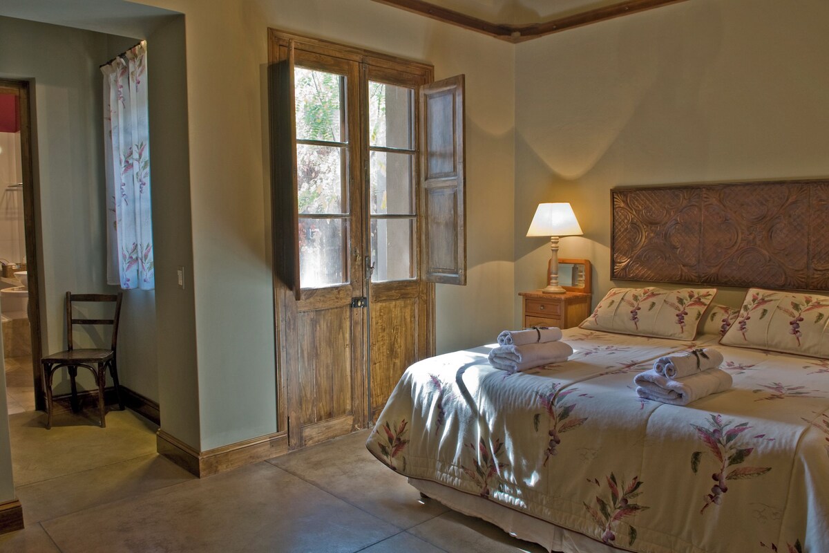 A bedroom with a bed, a nightstand, a lamp, a chair, and a door with a window.