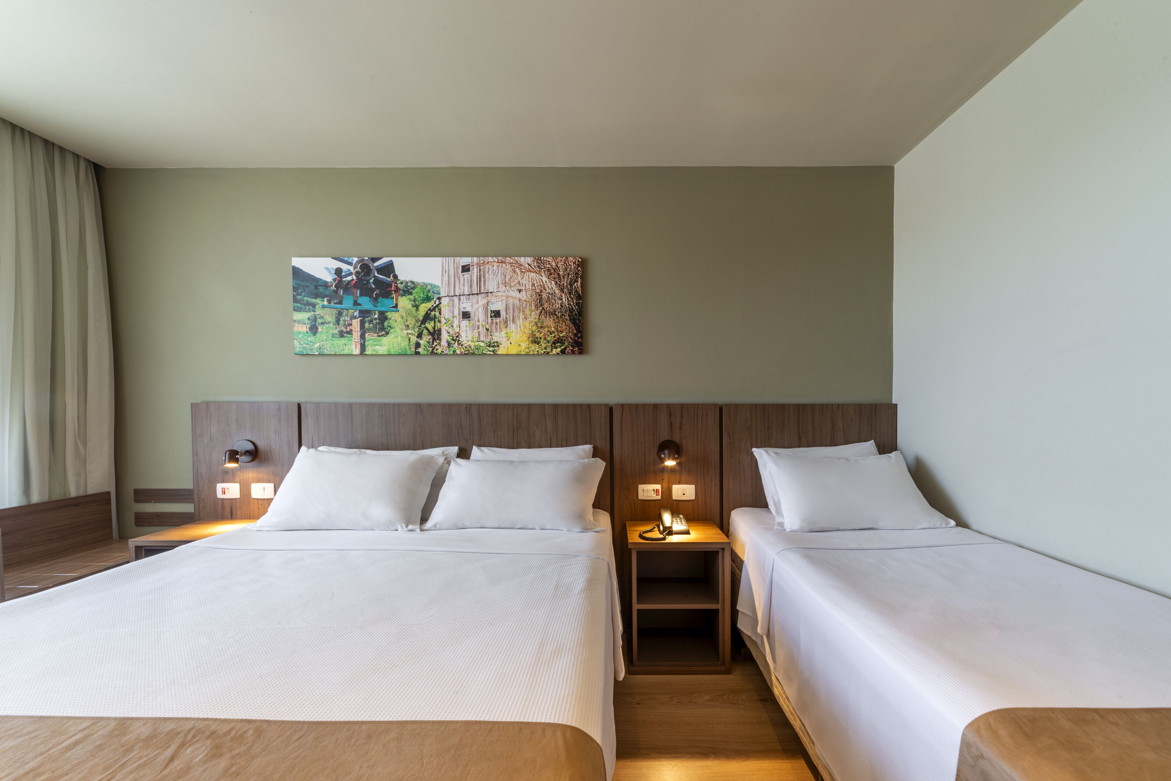 Quarto de hotel com duas camas, uma mesa de cabeceira com abajur e um quadro na parede.