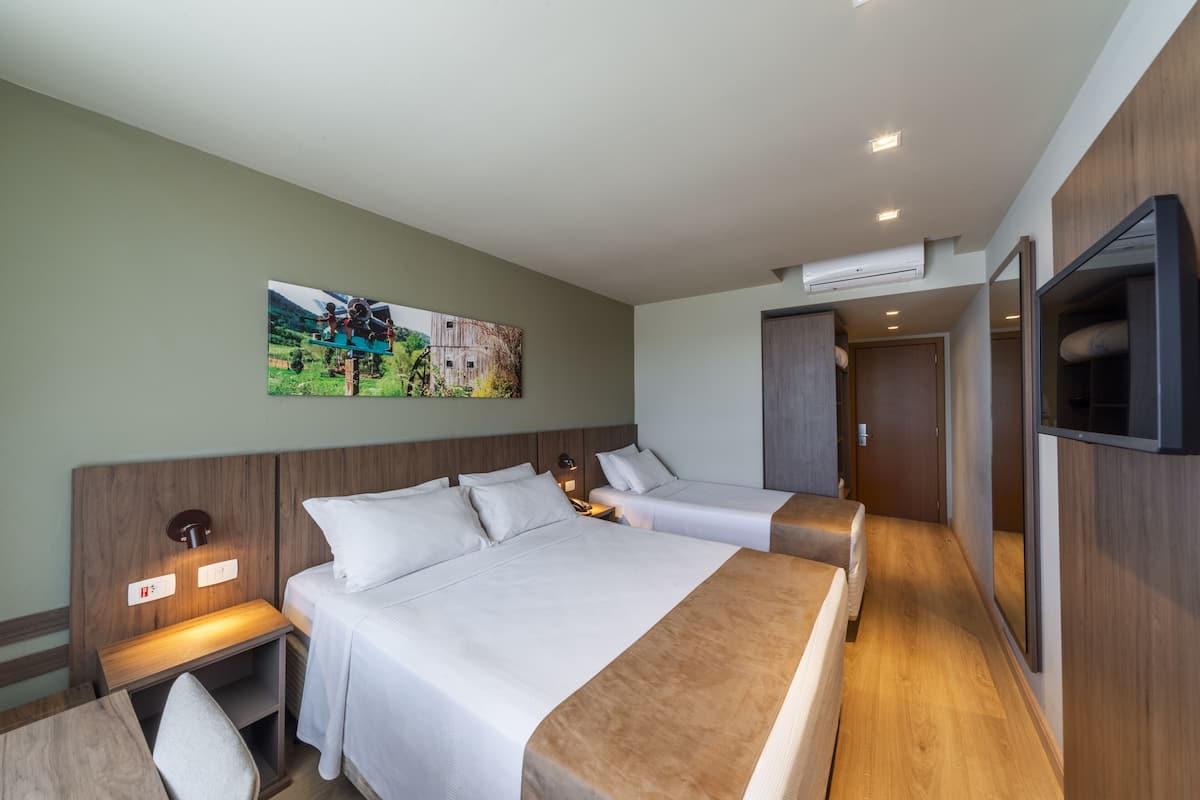 Een hotelkamer met twee bedden, een houten hoofdbord, een aan de muur bevestigde televisie en een schilderij van een polderlandschap.