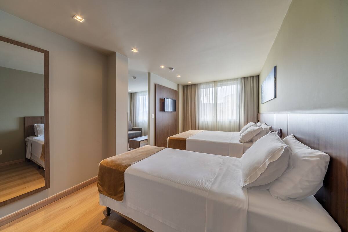 Een hotelkamer met twee bedden, een grote spiegel, een televisie en een houten vloer.