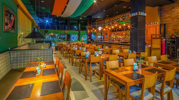 Een restaurant met meerdere houten tafels en stoelen, een bar met verschillende flessen, en een kerstboomdecoratie.
